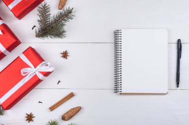 Beyaz ahşap arka planda xmas süslemeleri, kopya alanı ile üstten görünüm boş defter. Defter için istek listesi veya yapılacaklar listesi, kırmızı hediye kutuları, köknar ağacı dalları ile Noel arka plan. Düz yatıyordu