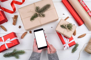 Eller ile mobil akıllı telefon ile app sunuda, kopya alanı boş perde. Noel hediyeleri kraft ve kırmızı ahşap arka plan üzerinde sarılı. Düz yatıyordu, en iyi görünüm. Uygulama şablonu sahte