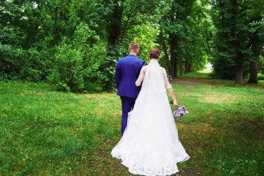 Tam uzunlukta vücut portresi Genç gelin ve damat park açık havada, arkadan görünüm içinde yeşil çimenlerin üzerinde yürüyüş. Mutlu evlilik çift, kopya alanı  