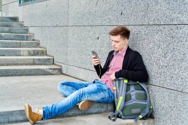 Merdivenlerde oturan ve cep telefonu kulaklık ile müzik dinlemek, internet'te sörf, geri kalan üniversite kampüsünde açık havada, kopya alanı olan öğrenci. Eğitim, dinlenmek ve rahatlamak kavramı