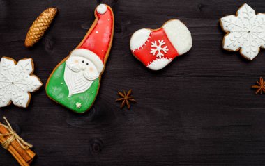 Ev yapımı gingerbread çerezleri üstten görünüm, koyu ahşap masa üzerine krema ile lay düz. Boder Noel Baba, kar tanesi, çorap, koni, tarçın ve anason yıldızlı ve ev, kopya alanı ile Noel arka plan