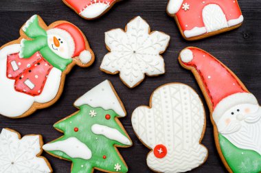 Üstten görünüm, koyu ahşap masa üzerine krema ile lezzetli ev yapımı gingerbread çerezleri lay düz. Noel Baba, kardan adam, kar tanesi, çorap, çam ağacı, mitten ve ev, kopya alanı ile Noel arka plan