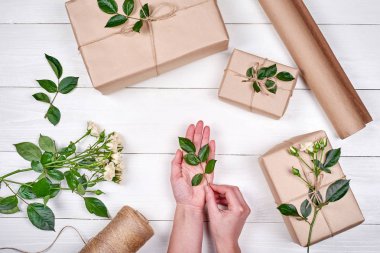 Yeşil yaprak ile elinde tutan kadın etrafında beyaz ahşap zemin üzerinde kopya alanı sunar. Holidaywrapping arka plan. Düz yatıyordu, en iyi görünüm. Hediye ambalaj arka plan