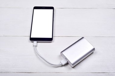 Hareket eden smartphone ile beyaz ahşap Resepsiyon arka planda, boş alan güç banka (pil banka) ile şarj beyaz boş perde. Üstten görünüm kopya alanı, düz ile yatıyordu. Teknoloji kavramı