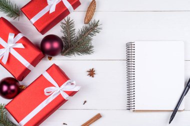 Beyaz ahşap arka planda xmas süslemeleri, kopya alanı ile üstten görünüm boş defter. Defter için istek listesi veya yapılacaklar listesi, kırmızı hediye kutuları, köknar ağacı dalları ile Noel arka plan. Düz yatıyordu