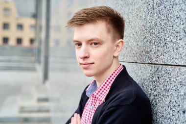 Gri taş duvara yakın duran ve geri kalan üniversite kampüsünde açık havada, kopya alanı olan yakışıklı erkek öğrenci portresi. Eğitim, dinlenmek ve rahatlamak, seyahat ve Turizm kavramı 