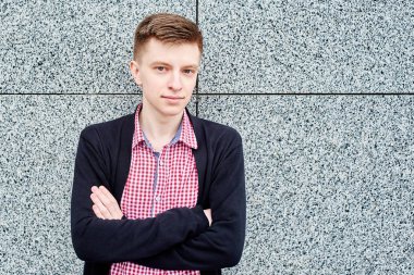 Gri taş duvar ve dinlenme açık havada, üniversite kampüsü içinde olan yakın çapraz ellerle kopya alanı ayakta yakışıklı erkek öğrenci portresi. Eğitim, dinlenmek ve rahatlamak, seyahat ve Turizm kavramı 