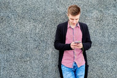 Taş duvara yakın duran ve kopya alanı cep telefonunda kulaklık, dinlenme açık havada, üniversite kampüsü içinde olması ile müzik dinlemek mutlu öğrenci. Eğitim, dinlenmek ve rahatlamak kavramı