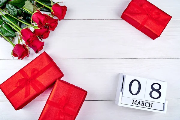Kırmızı hediye kutuları, güller ve beyaz ahşap arka planda, küp takvim metin için yer kopyalayın. Tarihi beyaz blok takvim 8 Mart kadın günler için sakla. Tebrik kartı. Üstten görünüm, düz yatıyordu