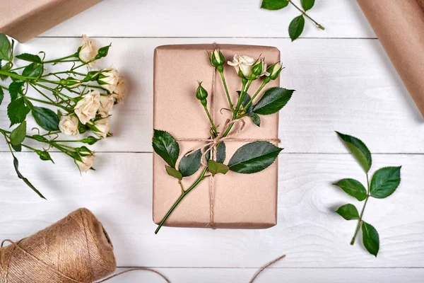 Gift wrapping background, copy space. Rolls of kraft wrapping paper, twine, branch of roses, gift box on wooden background, free space. Flat lay, top view. Womens Day, March 8, Mothers Day, Easter