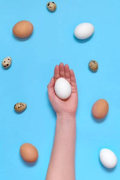 Woman holding white egg in hand with eggs on blue background, copy space. Healthy food concept. Top view, flat lay. Easter eggs. Happy Easter concept