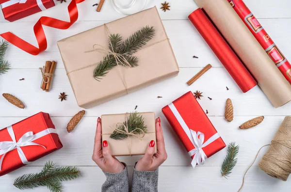 Christmas gift wrapping background. Female hands packaging christmas present wrapped in kraft paper; top view. Winter holidays concept; flat lay. Woman holding Christmas gift box