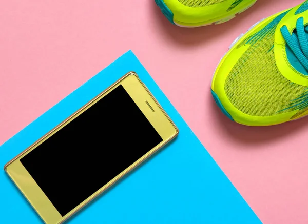 Pair of sport shoes and mobile cellphone on colorful background. New sneakers on pink and blue pastel background, copy space. Overhead shot of running shoes and smartphone. Top view, flat lay