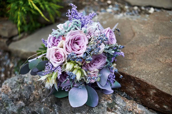 Close up of lush wedding bouquet of purple roses, violet flowers and leaves on stone background, copy space. Bridal bouquet outdoors. Greeting card