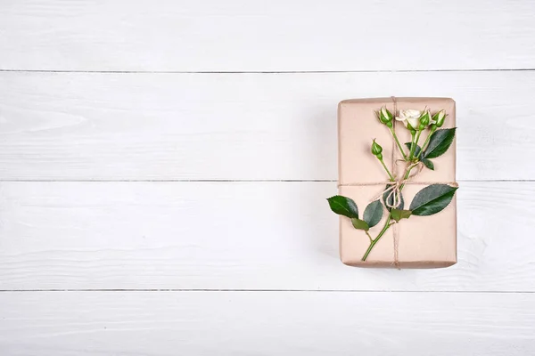 Top view of gift box with branch of fresh roses on wooden table, copy space. Holiday background, sale, shopping. Gift wrapping. Greeting card for Valentines Day, Womans Day, Mothers Day, flat lay