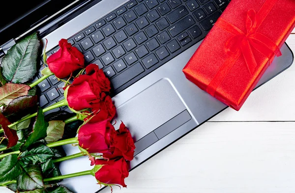 Top view of bouquet of red roses and red gift box on keybord of open laptop computer. Greeting card for Valentines Day, Womans Day, Mothers Day. Flat lay
