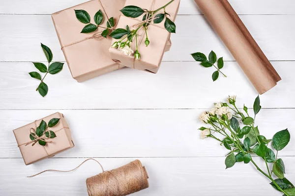 Gift wrapping background. Rolls of kraft wrapping paper, twine, branch of roses, gift boxes on wooden background, copy space. Flat lay, top view. Womens Day, March 8, Mothers Day, Easter, spring