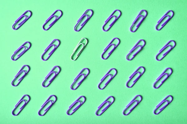 One white paperclip among violet paper clips on turquoise background, copy space. Top view, flat lay. Back to school, business concept. Individuality, outstanding, uniqueness, think different, leadership