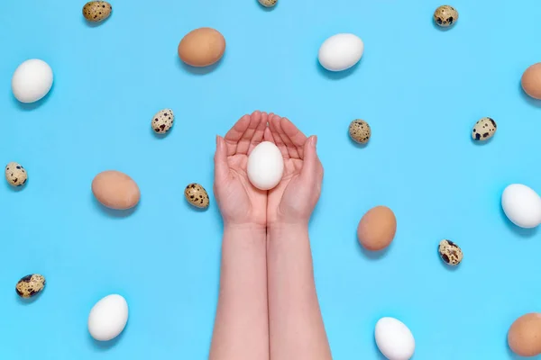 Woman holding white egg in hands with eggs on blue background, copy space. Healthy food concept. Top view, flat lay. Easter eggs. Happy Easter concept