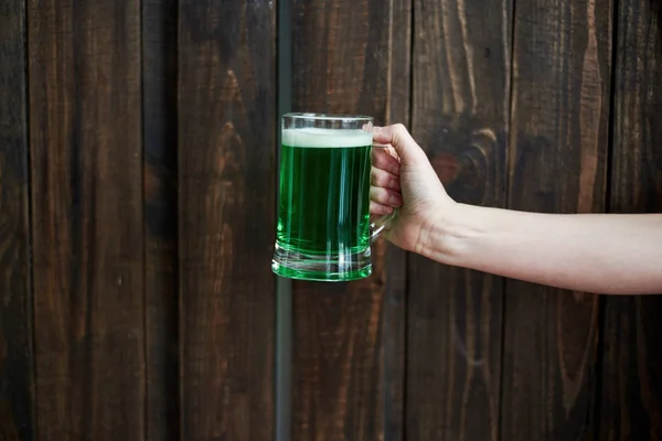 Woman holding mug of green beer on wooden background, copy space. Female hand holding glass of beer in pub. Greeting card for St. Patricks Day, March 17