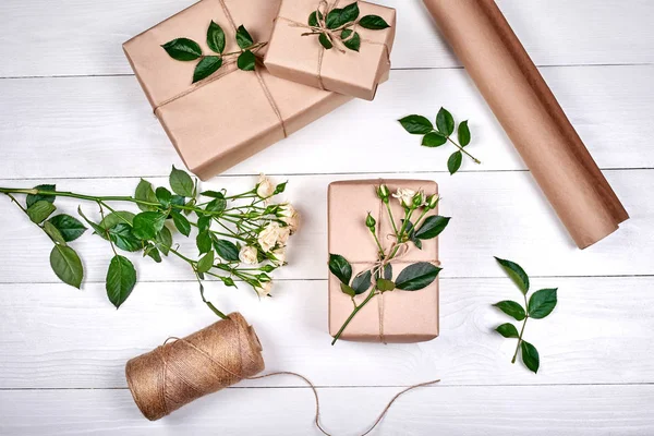 Gift wrapping background. Rolls of kraft wrapping paper, twine, branch of roses, gift boxes on wooden background, copy space. Flat lay, top view. Womens Day, March 8, Mothers Day, Easter, spring
