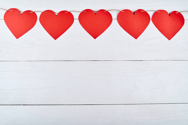 Red paper hearts garland on white wooden background, copy space for text. Greeting card mockup for Saint Valentines Day. Top view, flat lay. Symbol of love, free space. Love, wedding concept