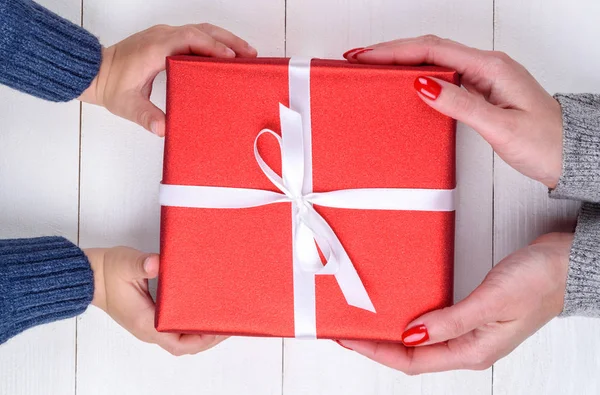 Son giving christmas gift to mum, top view. Holidays, present, childhood and happiness concept. Close up of child and mother hands with gift box on white background. Christmas family traditions