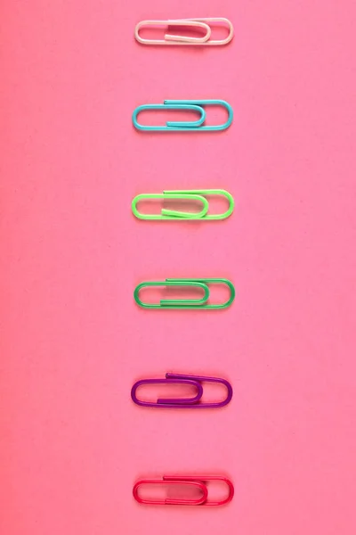 Colorful paper clips isolated on pink background, close up, copy space. Top view, flat lay. Back to school, college, education concept. White, tuqruois, yellow, green, violet, pink paperclips