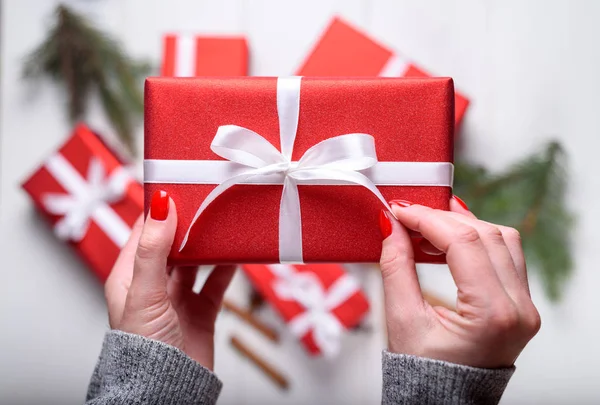 Kırmızı Noel hediyesi Beyaz ahşap arka plan üstüne tutan genç kadın el kapatın. Noel arka plan kırmızı hediye kutuları ile. Düz yatıyordu, en iyi görünümü