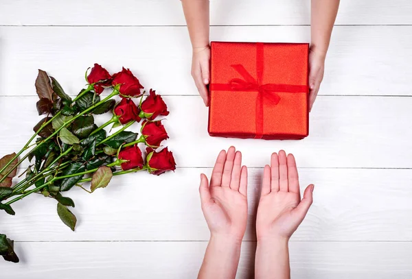 Son giving gift box and flowers to mum, top view. Holidays, present, childhood concept. Close up of child and mother hands with gift box on white background. Mothers day, Womens day, March 8, birthday
