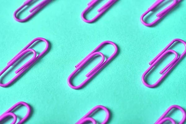 Violet paper clips isolated on turquois background, close up, copy space. Top view, flat lay. Back to school, college, education concept