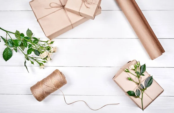 Gift wrapping background, copy space. Rolls of kraft wrapping paper, twine, branch of roses, gift boxes on wooden background, free space. Flat lay, top view. Womens Day, March 8, Easter, spring