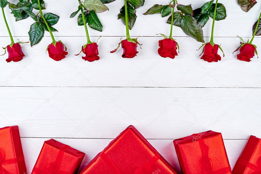 Top view of red roses and gift boxes border on white wooden background, copy space. Greeting card mockup for Saint Valentines Day, Womans Day (March 8), Mothers Day, flat lay. Love concept