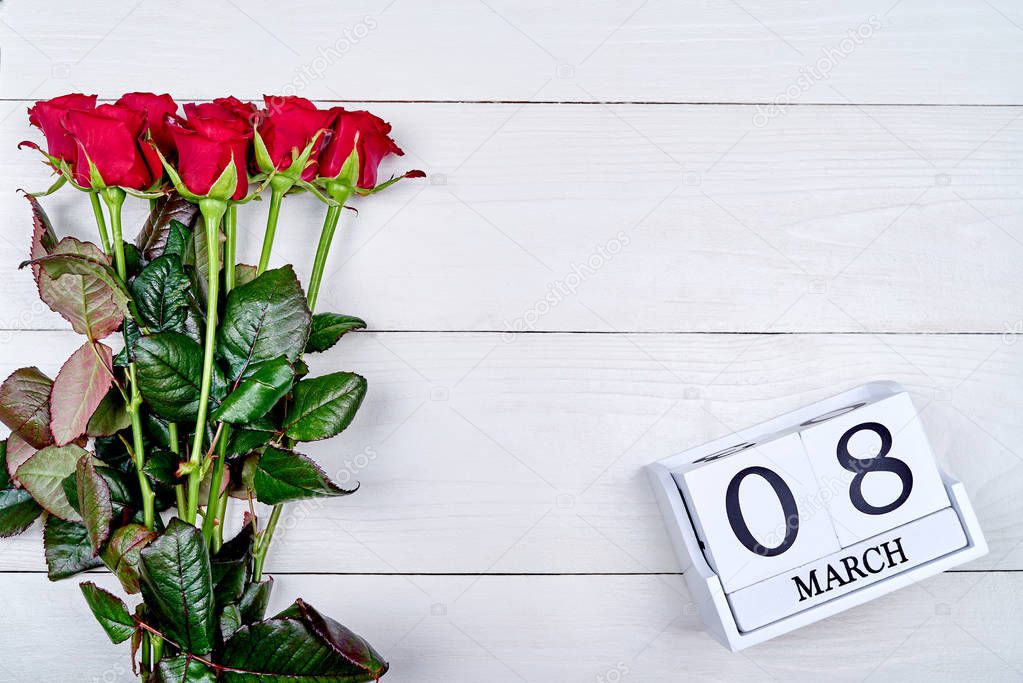 Bouquet of red roses with cube calendar on white wooden background, copy space for text. Save the date white block calendar for International Women's Day, March 8. Greeting card. Top view, flat lay