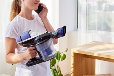 Elektrikli süpürge tutarak ve cep telefonundan, kopya alanı söz beyaz gömlekli güzel ve genç birbayan. Ev işleri, bahar-cleanig ve ev işleri kavramı. House hijyen, temizlik Vakum tekniği 