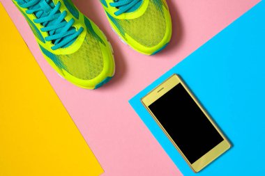 Çift spor ayakkabı ve renkli arka plan üzerinde Mobil cep telefonu. Pastel arka plan, kopya alanı üzerinde yeni spor ayakkabıları. Genel gider atış koşu ayakkabıları ve smartphone. Üstten görünüm, düz yatıyordu