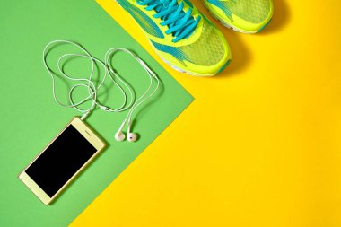 Çift spor ayakkabı ve renkli arka plan üzerinde kulaklık ile mobil cep telefonu. Yeşil ve sarı arka plan, kopya alanı üzerinde yeni spor ayakkabıları. Genel gider atış koşu ayakkabıları ve smartphone. Üstten görünüm, düz yatıyordu