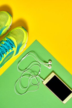 Çift spor ayakkabı ve renkli arka plan üzerinde kulaklık ile mobil cep telefonu. Yeşil ve sarı arka plan, kopya alanı üzerinde yeni spor ayakkabıları. Genel gider atış koşu ayakkabıları ve smartphone. Üstten görünüm, düz yatıyordu