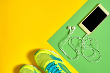 Çift spor ayakkabı ve renkli arka plan üzerinde kulaklık ile mobil cep telefonu. Yeşil ve sarı arka plan, kopya alanı üzerinde yeni spor ayakkabıları. Koşu ayakkabıları ve smartphone. Spor kavram. Üstten görünüm, düz yatıyordu