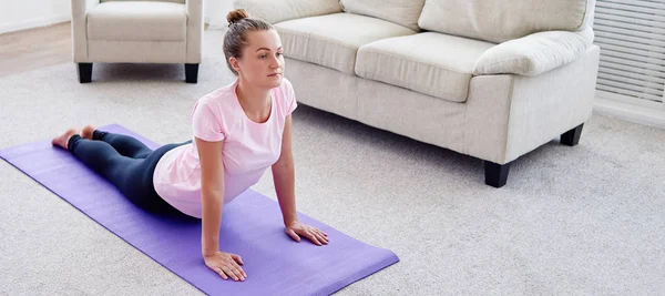 Portrait of young woman practicing yoga at home indoor, copy space. Girl practicing cobra pose, full length. Relaxing and doing yoga. Wellness and healthy lifestyle. Bhujangasana