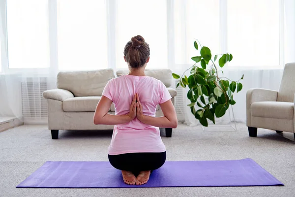 Young woman practicing yoga with namaste behind back at home indoor. Girl doing reverse prayer pose, back and shoulders stretching, working out, copy space. Healthy lifestyle