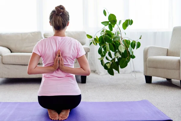 Young woman practicing yoga with namaste behind back at home indoor. Girl doing reverse prayer pose, back and shoulders stretching, working out, copy space. Healthy lifestyle