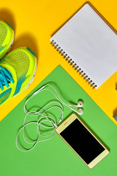 Sports equipment with shoes, skipping rope, blank notebook and mobile cellphone with earphones on colorful background. Top view, flat lay. Sport, fitness concept, healthy lifestyle