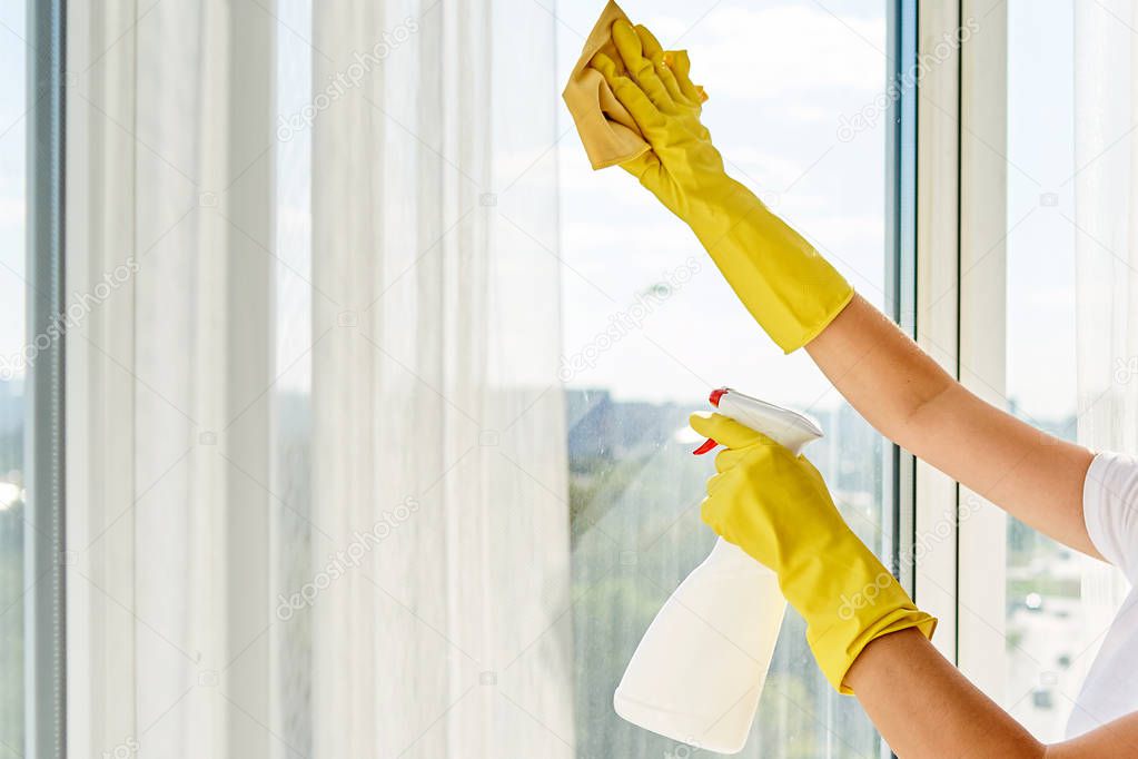 Close up of woman in yellow rubber gloves cleaning window with cleanser spray and yellow rag at home or office, copy space, back view. People, housework and housekeeping concept