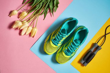 Çift spor ayakkabı, ip ve lale pastel renkli arka plan üzerinde atlama. Pembe, mavi ve sarı kağıt, kopya alanı üzerinde yeni spor ayakkabıları. Ayak çalışan genel gider atış giymek. Üstten görünüm, düz yatıyordu