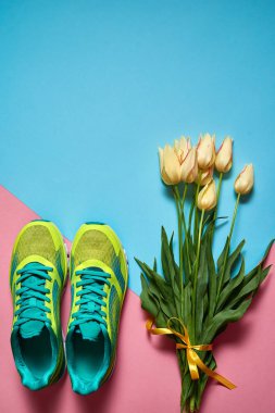 Çift spor ayakkabı ve pastel renkli arka plan üzerinde sarı lale buketi. Pembe ve mavi kağıt, kopya alanı üzerinde yeni spor ayakkabıları. Ayak çalışan genel gider atış giymek. Üstten görünüm, düz yatıyordu