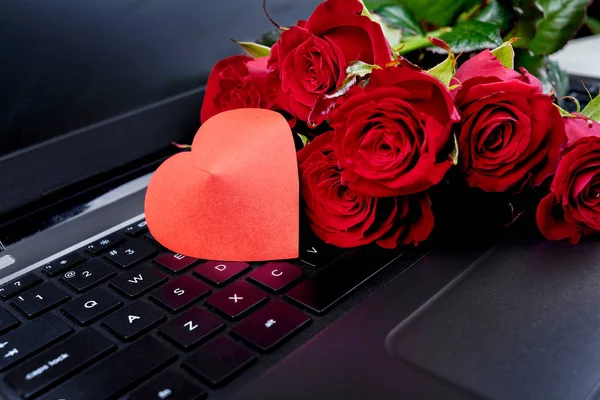 Bouquet of red roses and paper heart on keyboard of open laptop computer, copy space. Greeting card for Valentines Day, Womens Day, Mothers Day. Love concept. Top view, flat lay