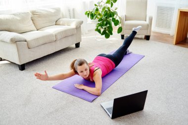 Dizüstü bilgisayarda, kopya alanı Eğitim Online egzersiz için sırt üstü yere vasıl ev, yapmak güzel ve genç birbayan. Tam uzunlukta portre. Çalışma dışarı egzersiz yoga, pilates,