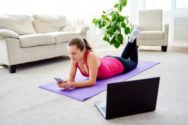 Mat katta ve evde, Mobil cep telefonu kullanarak kopya alanı rahatlatıcı eşofman mutlu gülümseyen genç kadın. Tam uzunlukta vücut. Spor, sağlıklı yaşam biçimi kavramı 