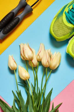 Çift spor ayakkabı, pastel renkli arka plan üzerinde ip ve lale buketi atlanıyor. Pembe, mavi ve sarı kağıt, kopya alanı üzerinde yeni spor ayakkabıları. Ayak çalışan genel gider atış giymek. Üstten görünüm, düz yatıyordu